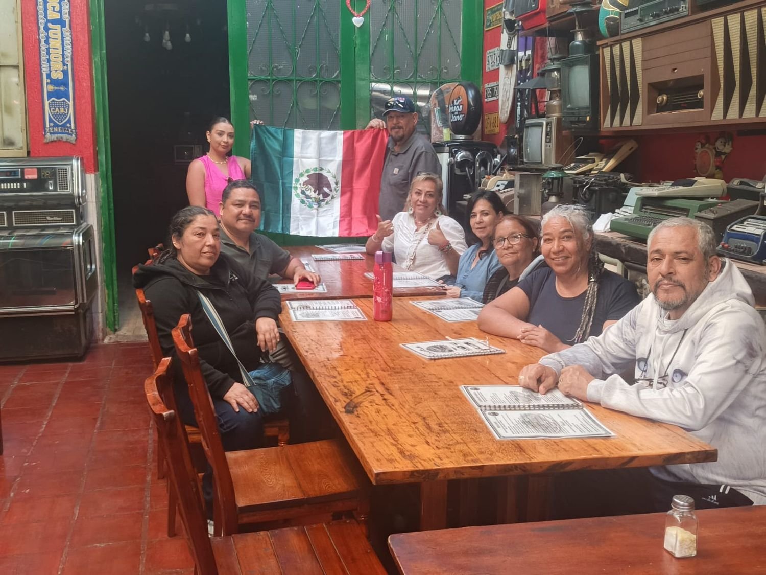 Grupo de viajeros cenando, con bandera de México de fondo